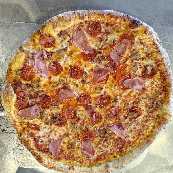 A freshly baked pizza with pepperoni, ham, and sausage on a metal peel.