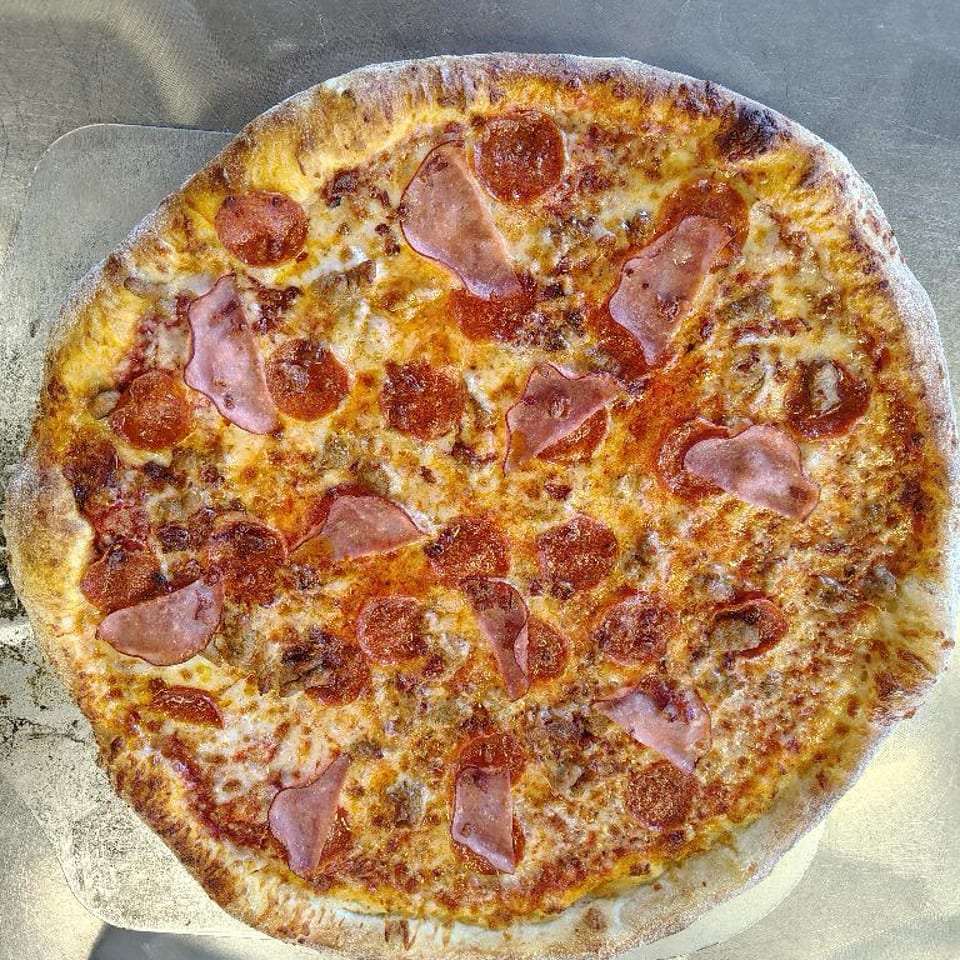 A freshly baked pizza with pepperoni, ham, and sausage on a metal peel.