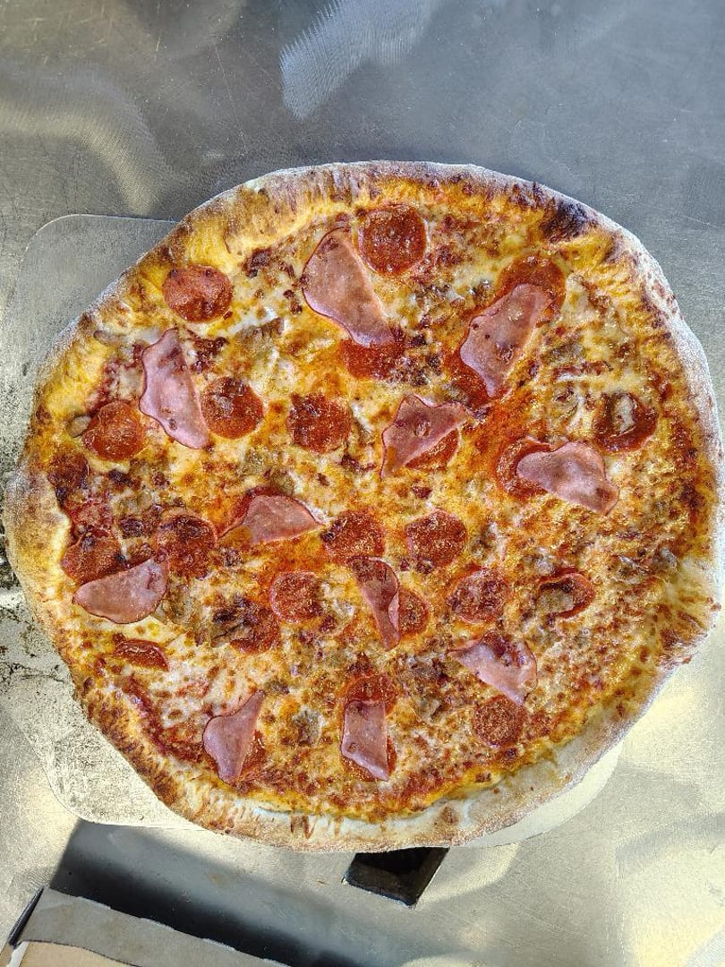 A freshly baked pizza with pepperoni, ham, and sausage on a metal peel.