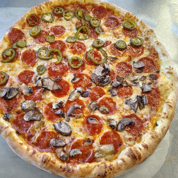 A whole pepperoni pizza with mushrooms on one half and jalapeños on the other.