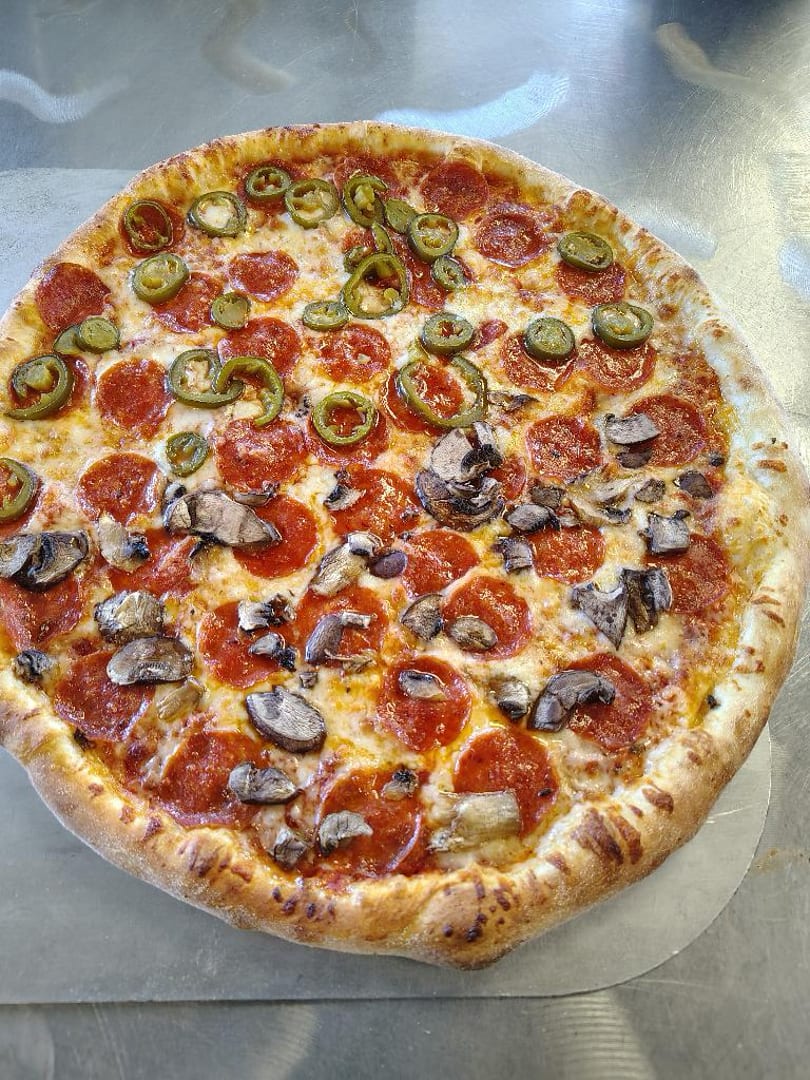 A whole pepperoni pizza with mushrooms on one half and jalapeños on the other.