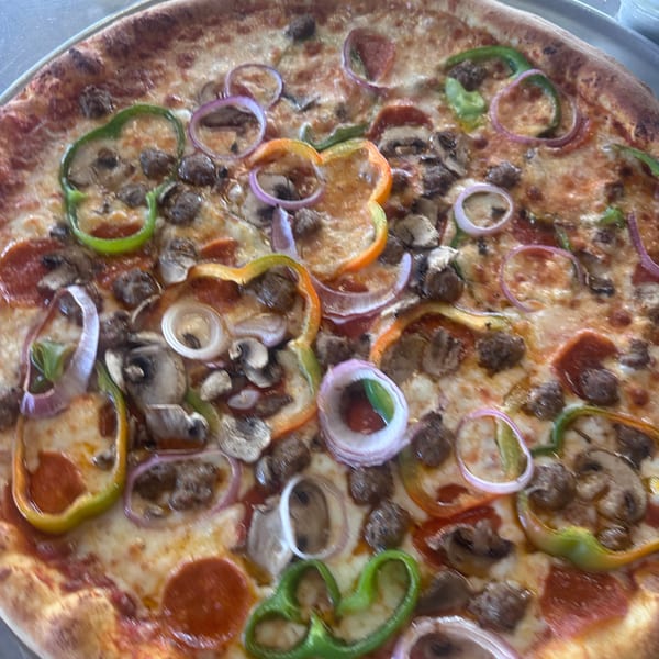 A whole pizza with pepperoni, sausage, mushrooms, green peppers, and red onions on a metal tray.