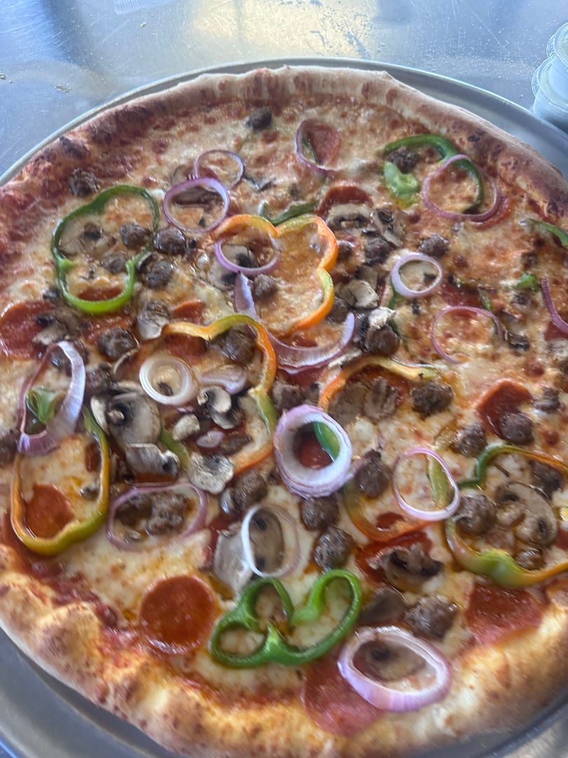 A whole pizza with pepperoni, sausage, mushrooms, green peppers, and red onions on a metal tray.